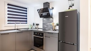 Une cuisine moderne équipée d’un four encastré, d’un réfrigérateur et d’une fenêtre avec des stores.