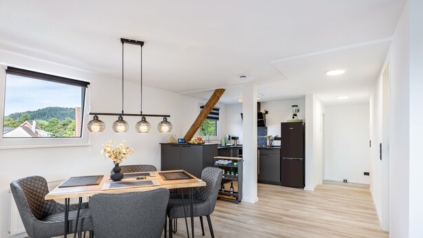 Une cuisine moderne avec une table et des chaises en bois, un four encastré et une vue sur l’extérieur.