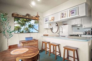 Cocina compacta con isla central, muebles blancos y un amplio ventanal con vistas tropicales.