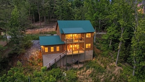 A two-story log cabin with a green roof, surrounded by dense forest. - Heavenly Splash: Dive Into Paradise (Sevierville)