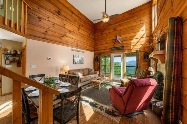 A cozy cabin interior with a dining area, a sofa, a red armchair, and a view through the door.