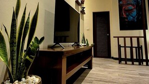 A modern living room with a flat-screen TV, wooden entertainment unit, potted plants, and artwork on the walls. - Sea View Apartment near Secret Beach, Koh Phangan (ตำบลเกาะพะงัน)