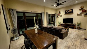 A dining area with a wooden table, chairs, and a fan. There is a sofa and a TV in the living area. - Sea View Apartment near Secret Beach, Koh Phangan (ตำบลเกาะพะงัน)