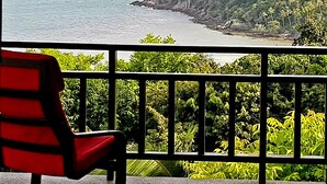 A balcony with a red chair overlooking a coastal view with a rocky island and dense greenery. - Sea View Apartment near Secret Beach, Koh Phangan (ตำบลเกาะพะงัน)