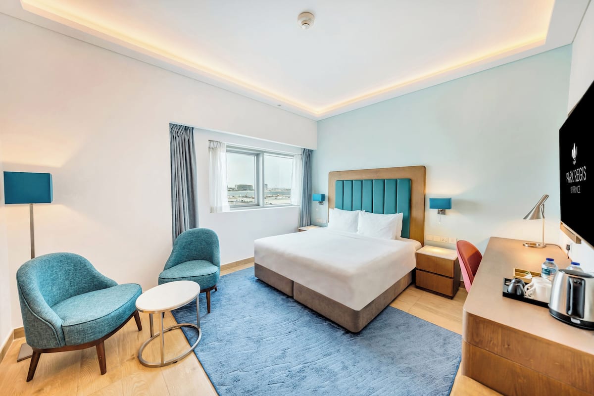 A hotel room with a large bed, two chairs, a small table, a desk with a lamp, and a TV.
