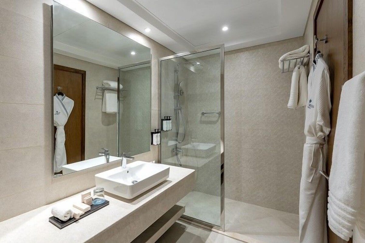 Un baño moderno con ducha de vidrio, un espejo grande y un tocador con lavamanos y barra para toallas.