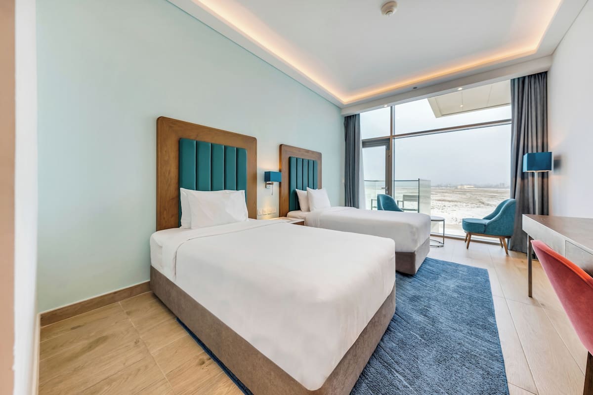 A hotel room with two beds, a desk, and a view of the beach.