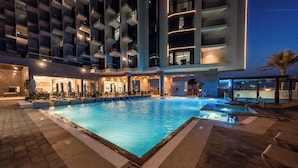 A swimming pool with a tiled deck, surrounded by a modern building with balconies and a well-lit entrance. - Sea Point Hotel (Dubai)