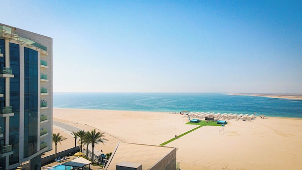 A beach view from a hotel balcony with a pool, beach umbrellas, and a clear sky. - Sea Point Hotel (Dubai)