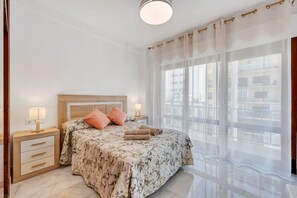 A bedroom with a bed, nightstands, a window with curtains, and a view of buildings. - Apartment 'Ángeles Center' with Balcony and Wi-Fi (Marbella)