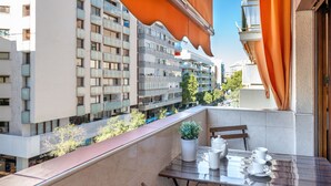 Een balkon met een tafel, stoelen, een bloempot en uitzicht op omliggende gebouwen.