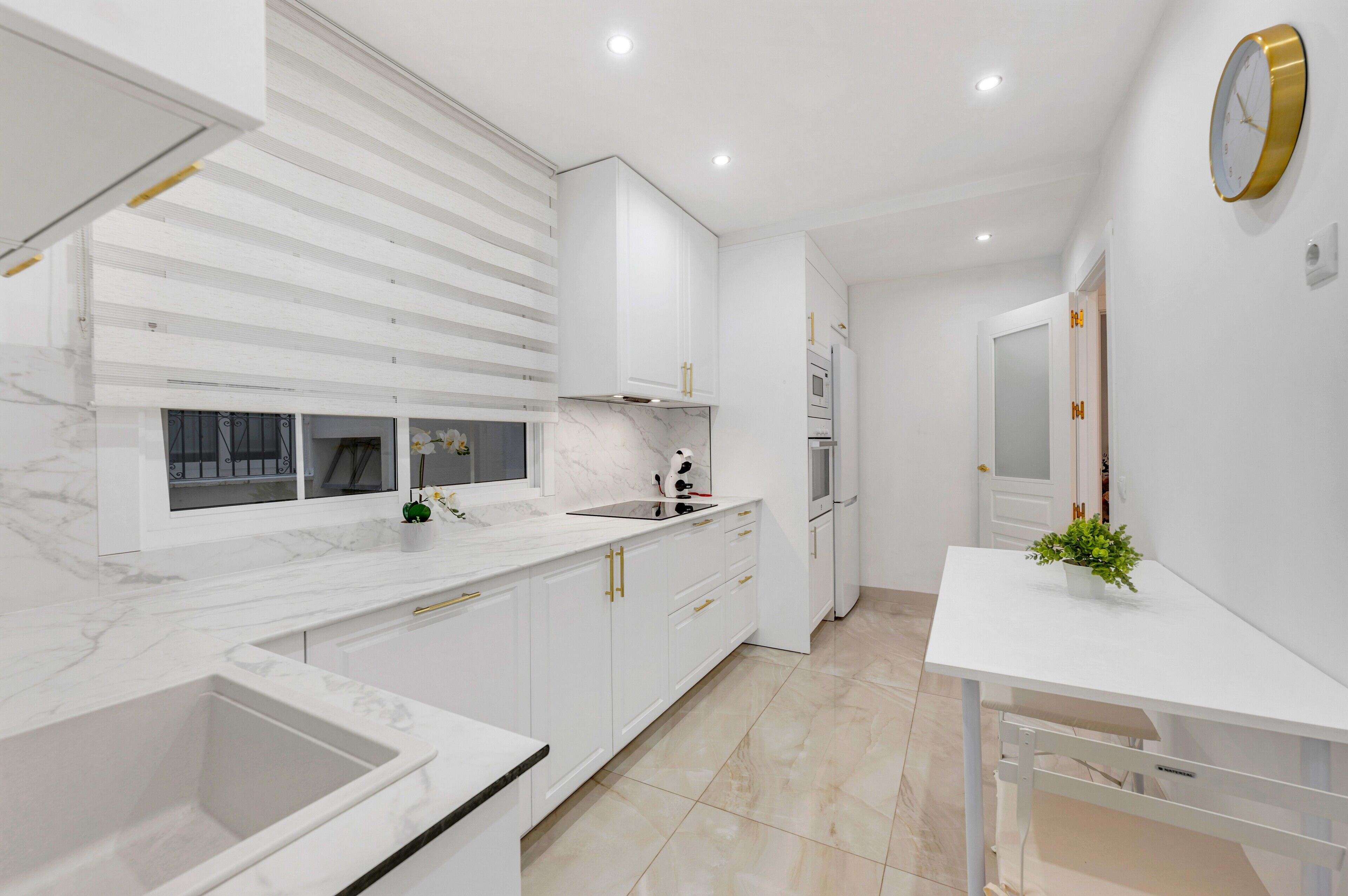 Una cocina moderna con armarios blancos, encimera de mármol y horno empotrado.