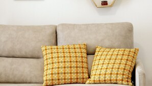A beige sofa with patterned cushions, a hexagonal wooden shelf with candles, and a floral painting on the wall. - CASA DAS COLMEIAS A haven of tranquillity, where nature reveals all its beauty. (Distrito de Évora)