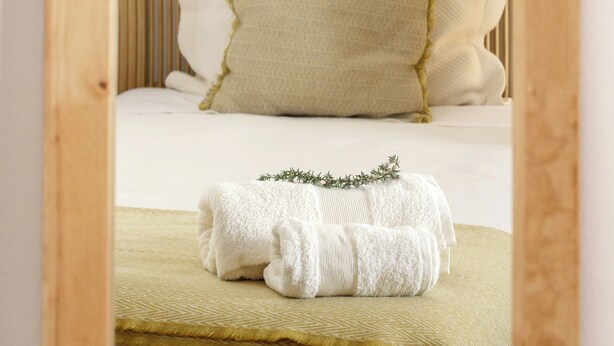 A neatly made bed with a green blanket and a white towel, a wooden headboard, and a white wall. - CASA DAS COLMEIAS A haven of tranquillity, where nature reveals all its beauty. (Distrito de Évora)