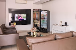 A modern living room with a flat-screen TV, a minibar, a seating area with leather sofas, and a decorative vase.