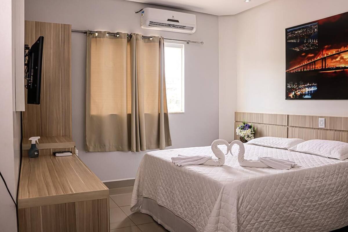 Ein Hotelzimmer mit Bett, Schreibtisch, Sprühflasche, Spiegel und Wandklimaanlage.