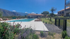 A pool area with lounge chairs, a building with a red-tiled roof, and mountains in the background. - Buena Vid- Cafayate- Between Wineries (Cafayate)