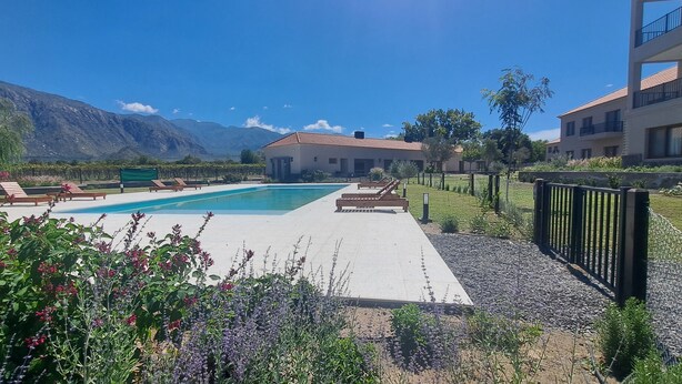 Un espace piscine avec des chaises longues, un bâtiment doté d’un toit recouvert de tuiles rouges et des montagnes en arrière-plan.