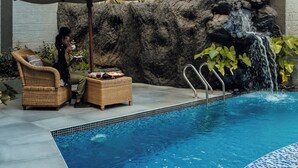 Zona de piscina amb cascada, mobiliari de vimet i vores de gres.