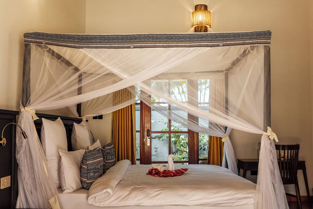 A four-poster bed with a canopy, a wooden floor, and a large woven ceiling light.