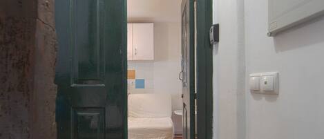 A narrow hallway with a wooden floor leading to a room with a bed and a white cabinet.