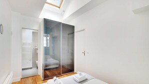 A modern hotel room with a glass door leading to a bathroom, a wooden floor, and a bed with towels. - Charming Apartment - 1br-6p - Sentier (Paris)