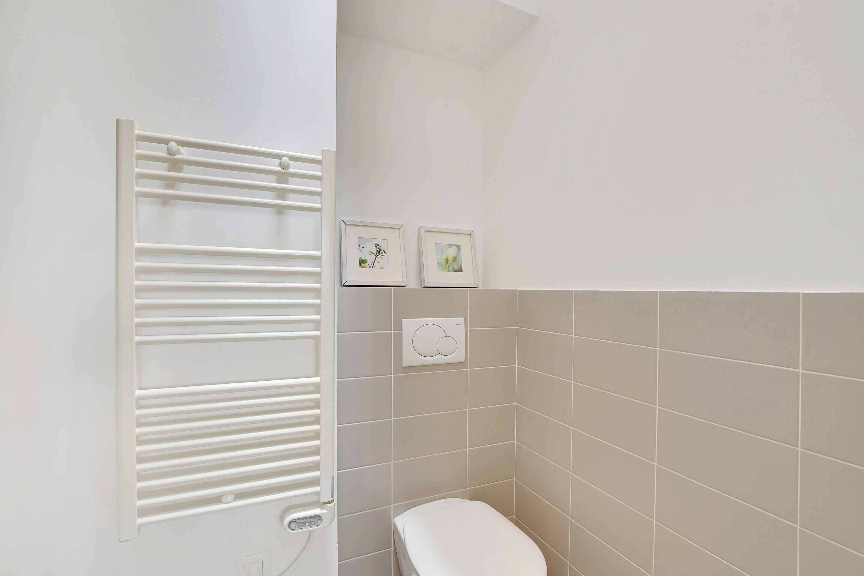 A bathroom with a white toilet, a towel rack, and two framed pictures on the wall.