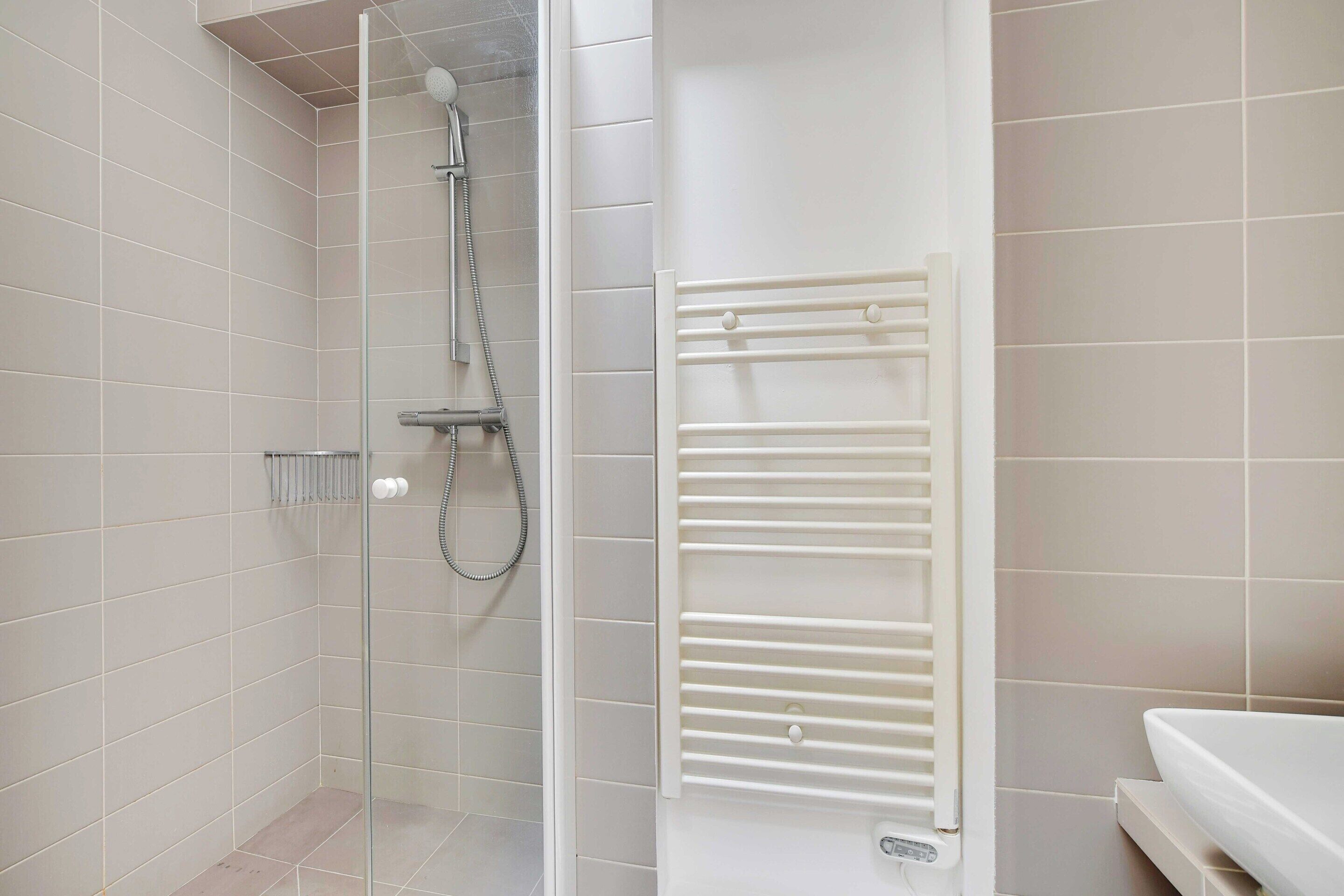 A modern bathroom with a glass-enclosed shower, a white bathtub, and a built-in towel rack.