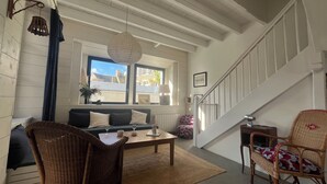 Un salon chaleureux avec un canapé, deux fauteuils en osier, une table basse et un escalier.