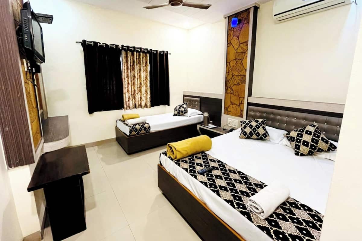 Une chambre d’hôtel avec deux lits, un téléviseur à écran plat, un climatiseur, un ventilateur de plafond et une fenêtre avec des rideaux.