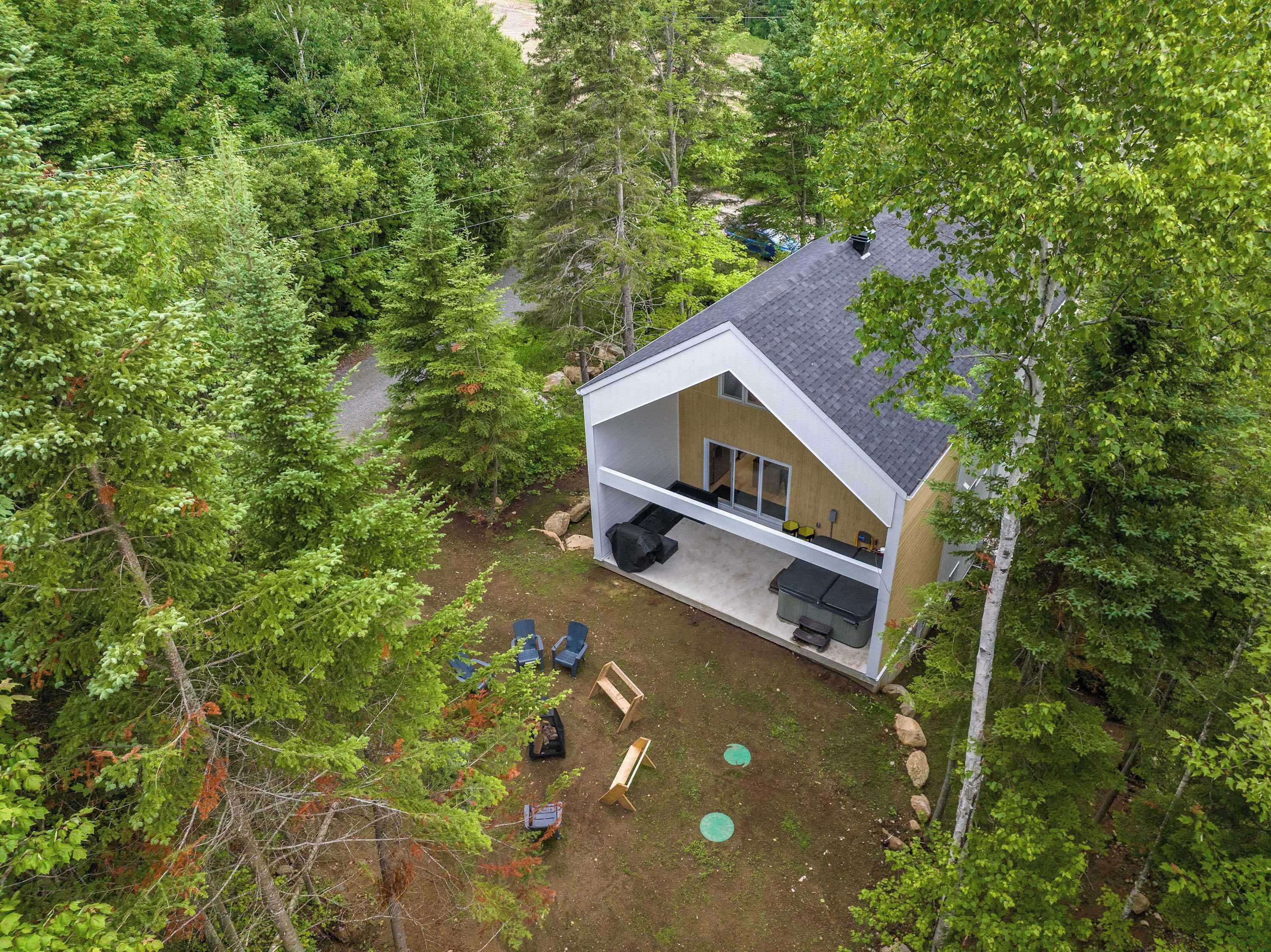 A modern house with a large deck, surrounded by dense forest.