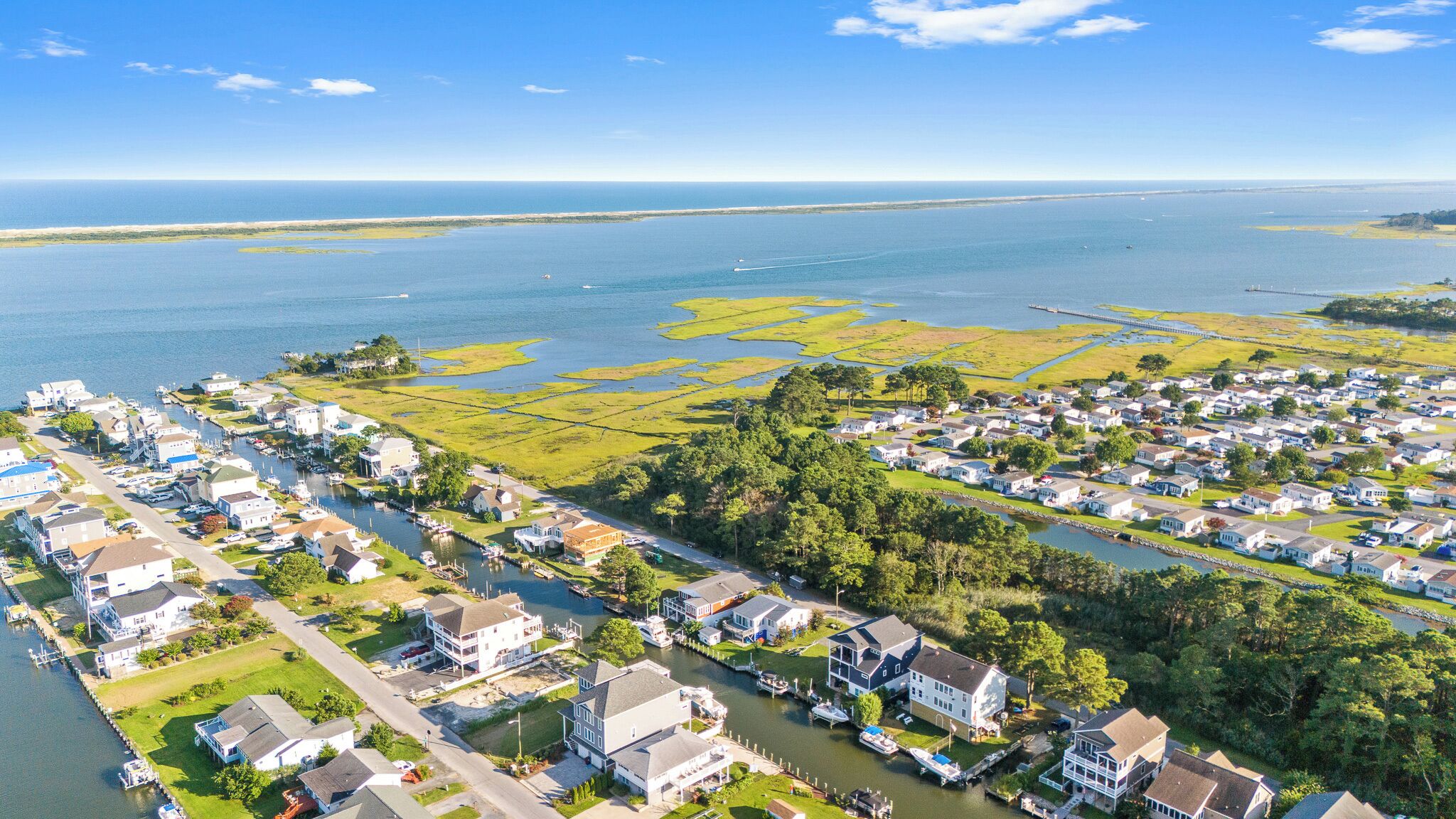 An aerial view of a coastal residential area with houses, a marina, and a large body of water.