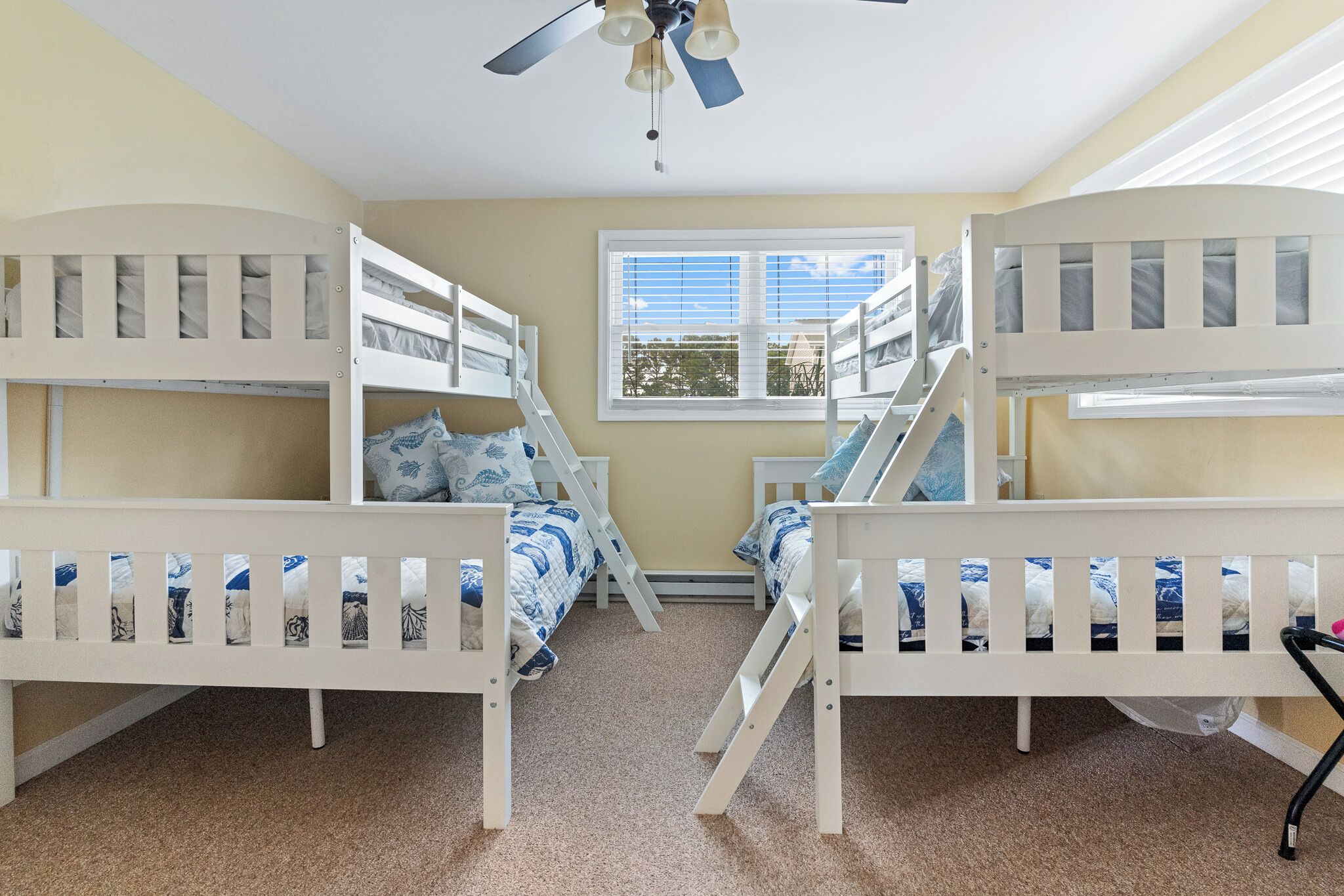 A room with bunk beds, a ceiling fan, and a window with blinds.