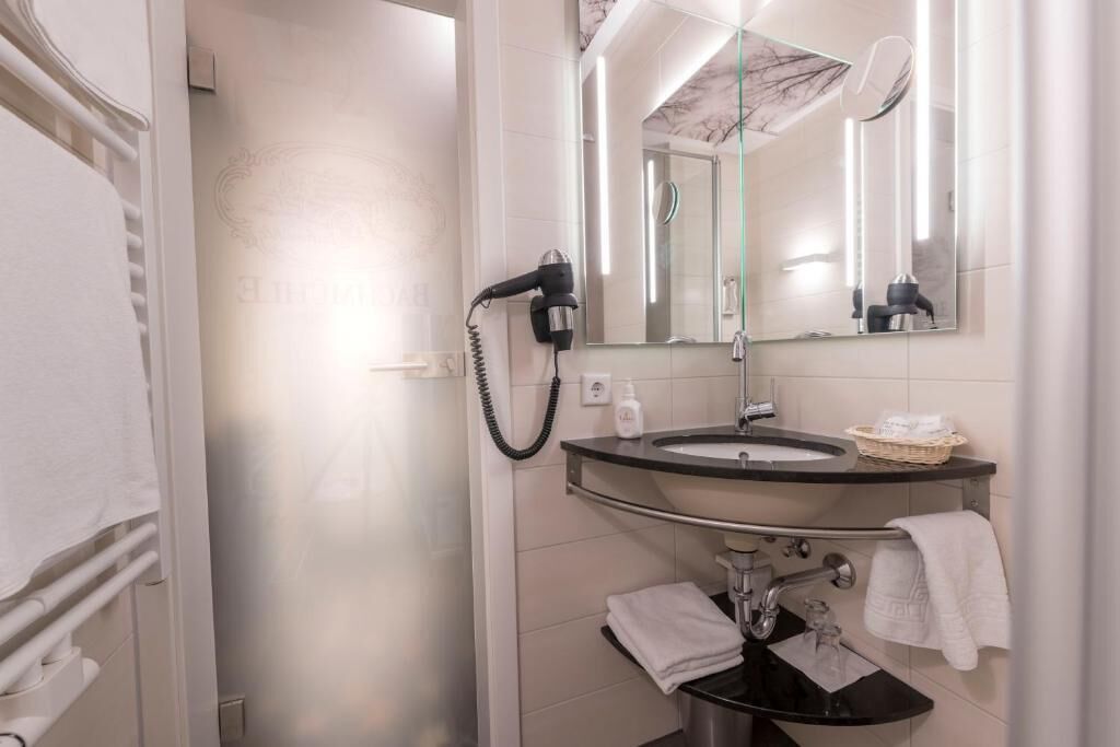 Une salle de bain moderne dotée d’une douche à parois de verre, d’un meuble-lavabo avec un évier et un miroir, et d’un sèche-cheveux fixé au mur.
