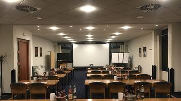 Un salón de conferencias con varias mesas, sillas y una gran pantalla al frente.