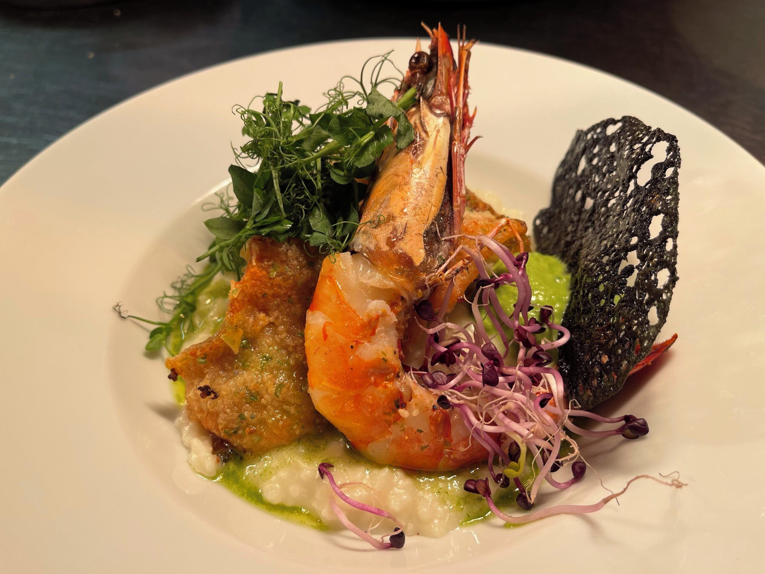 Un plato con camarones, vegetales verdes y una especie de pan.