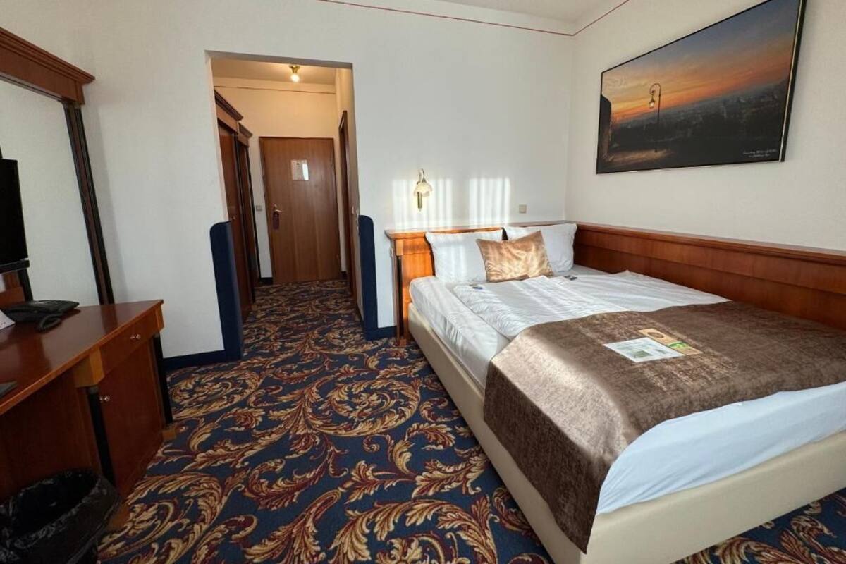 A hotel room with a large bed, a desk, a chair, and a painting on the wall.