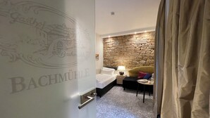 A hotel room with a stone wall, a bed with white linens, a small table with a lamp, and a chair. - Hotel-Restaurant Bachmühle (Fulda)