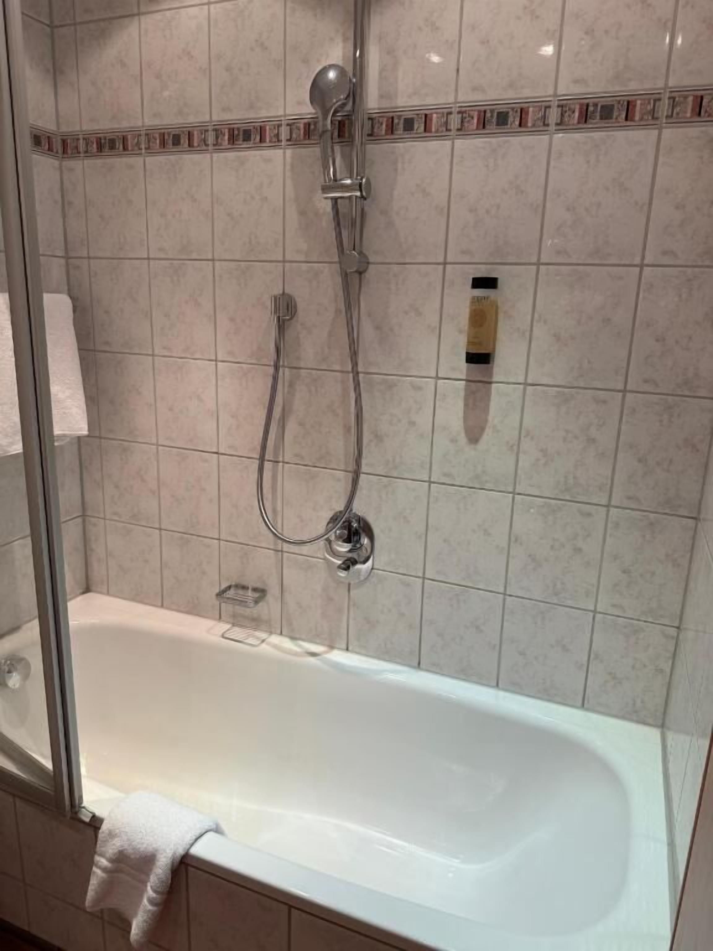 Un baño con bañera, ducha con cabezal de ducha manual y toallero.