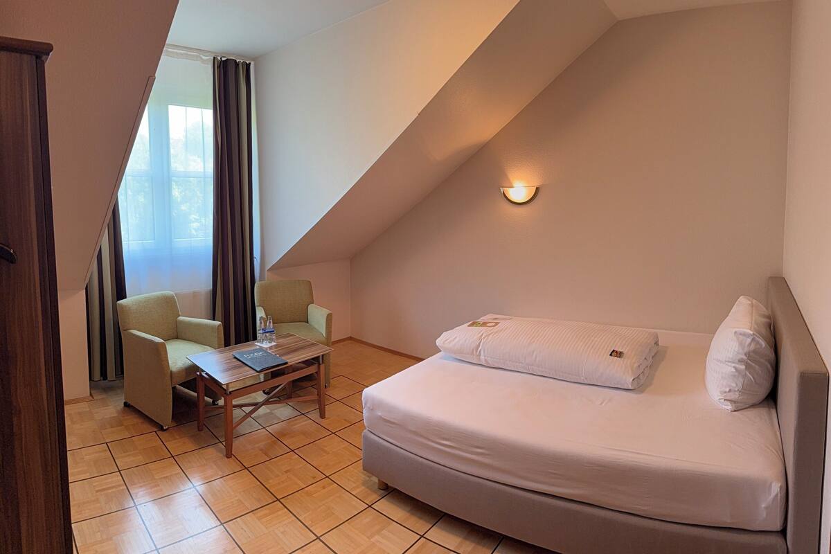 A cozy room with a curved sofa, a small table, and a chair. There is a window with curtains, a wall-mounted light, and a door.