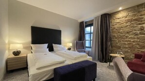 A hotel room with a large bed, a chair, a small table, and a stone wall. - Hotel-Restaurant Bachmühle (Fulda)