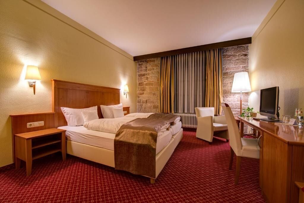 Habitación de hotel con cama, escritorio, silla, televisor y una pared decorativa de piedra.