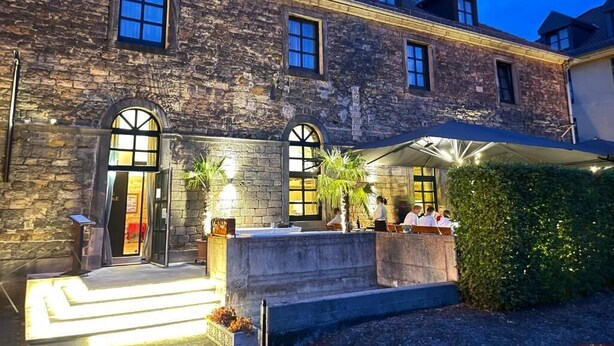 A stone building with a covered outdoor seating area and a staircase leading to the entrance. - Hotel-Restaurant Bachmühle (Fulda)