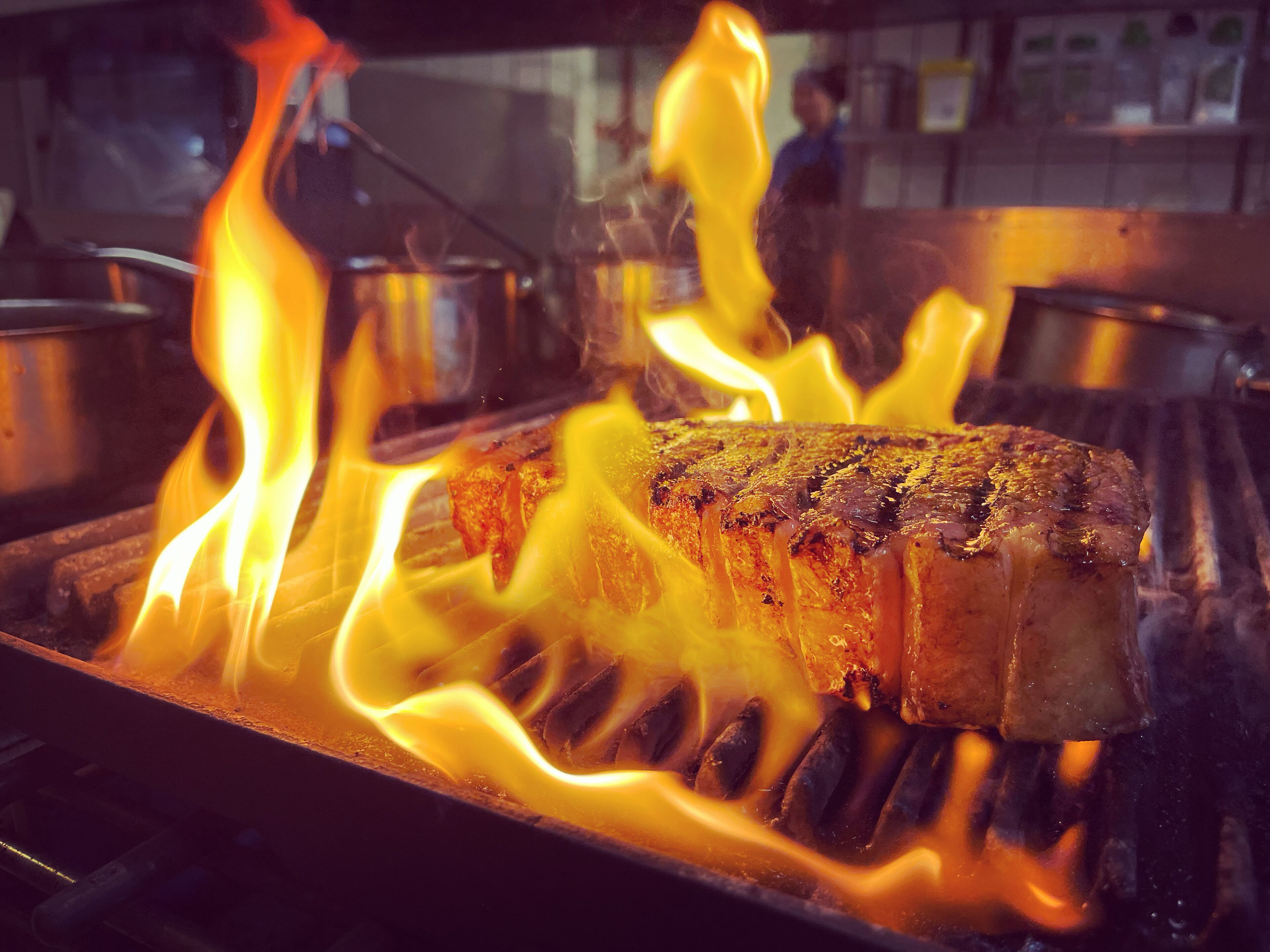 A steak being grilled over an open flame with visible flames.