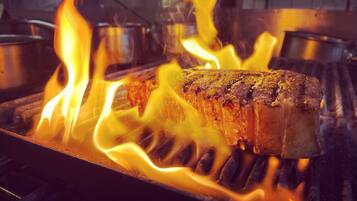 A steak being grilled over an open flame with visible flames.