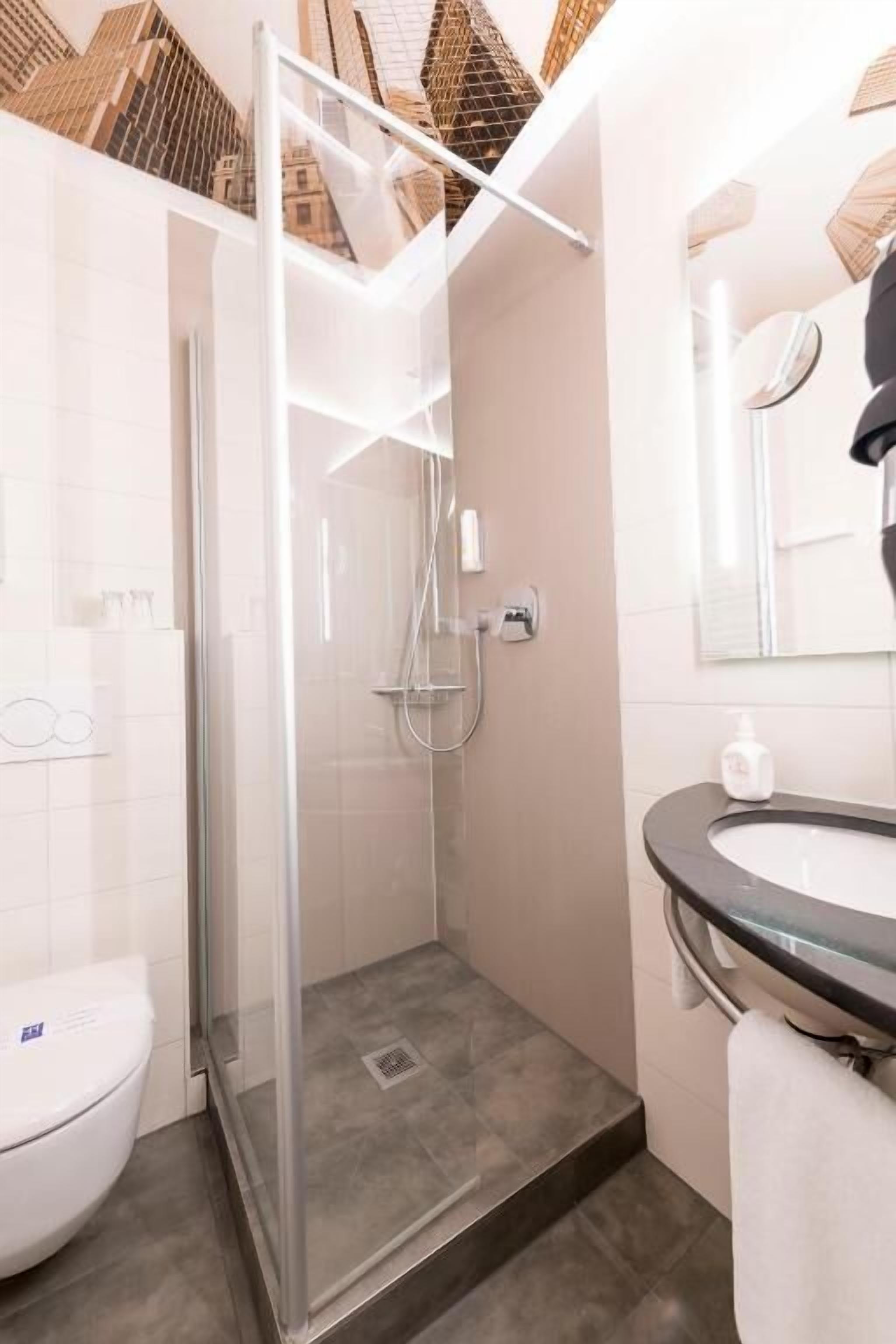 Un baño moderno con ducha de vidrio, inodoro blanco y lavamanos con encimera negra.