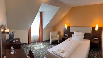Quarto de hotel com cama, escrivaninha com computador, cadeira e mesa pequena.