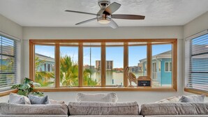A living room with a large window, a ceiling fan, and a view of a body of water and buildings. - 2BR Waterview Suite on Clearwater Beach w/ Pool (Clearwater)
