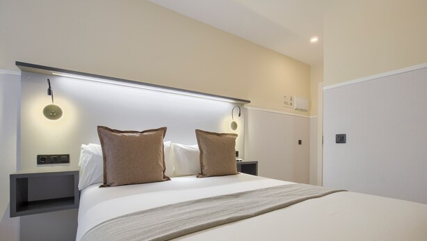 Una habitación de hotel moderna con una cama grande, dos mesitas de noche e iluminación empotrada.