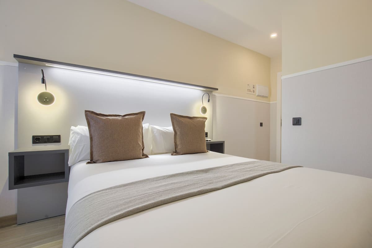 Una habitación de hotel moderna con una cama grande, dos mesitas de noche e iluminación empotrada.